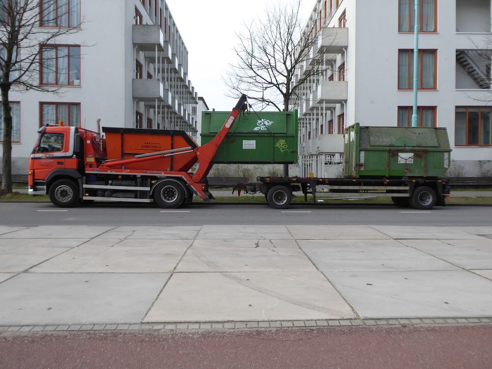 Dumpster being delivered by a hook-lift truck at a site